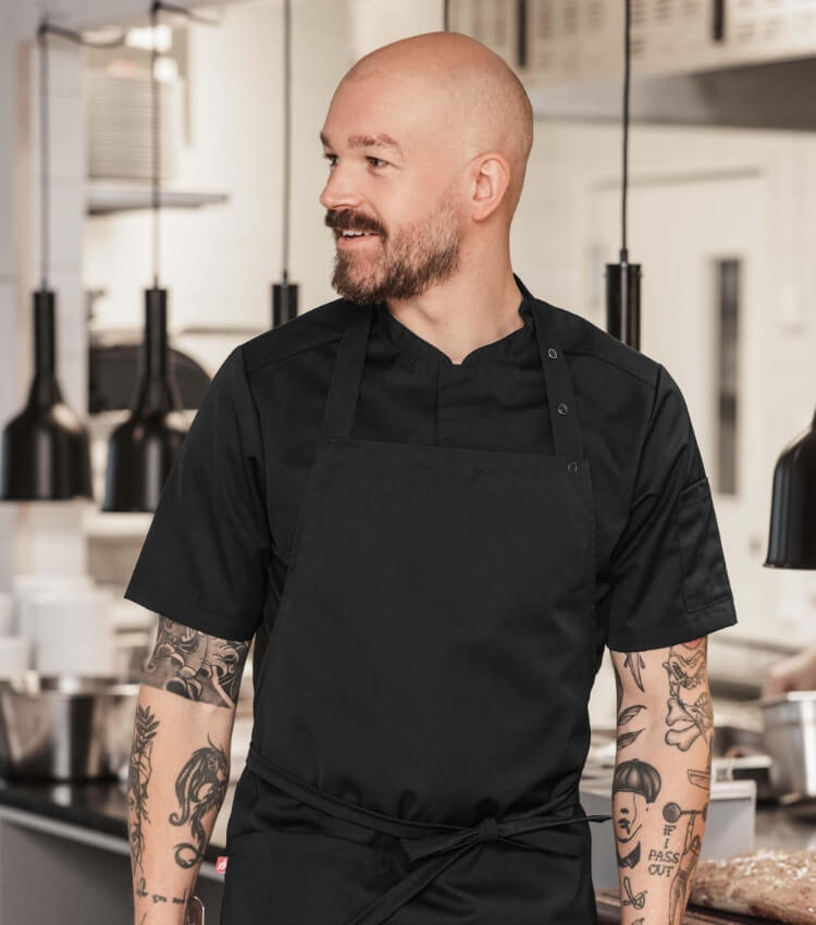 Kock klädd i svart förkläde och svart kockrock i restaurangkök.